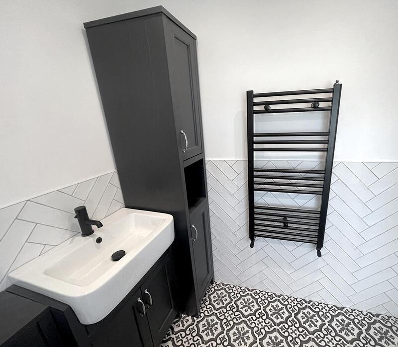 Intricate herringbone tiling design in classic white, laid up to dado height for an elegant and timeless finish with modern black towel radiator.