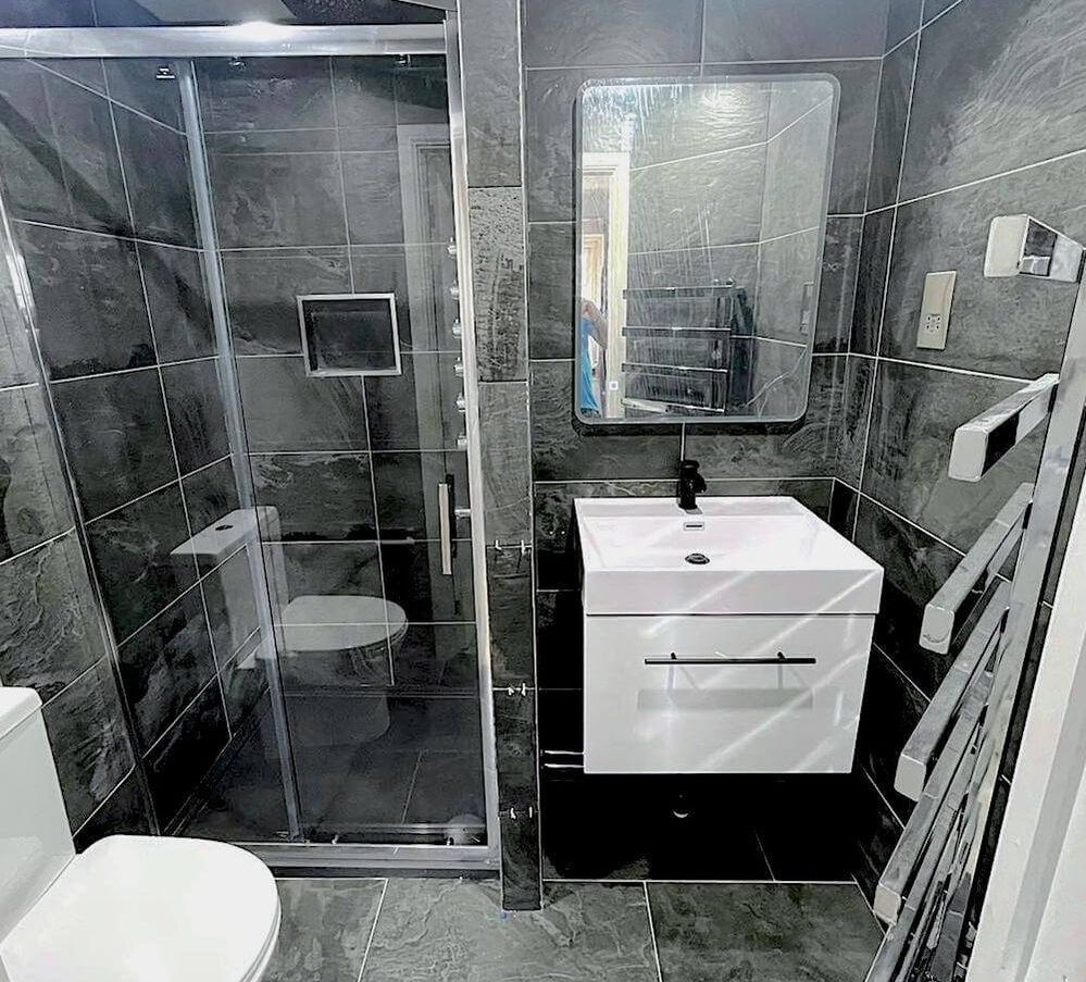 A sleek, modern bathroom renovation with greyscale tiles and black accessories and chrome bathroom towel rail in a newly renovated bathroom in St Albans